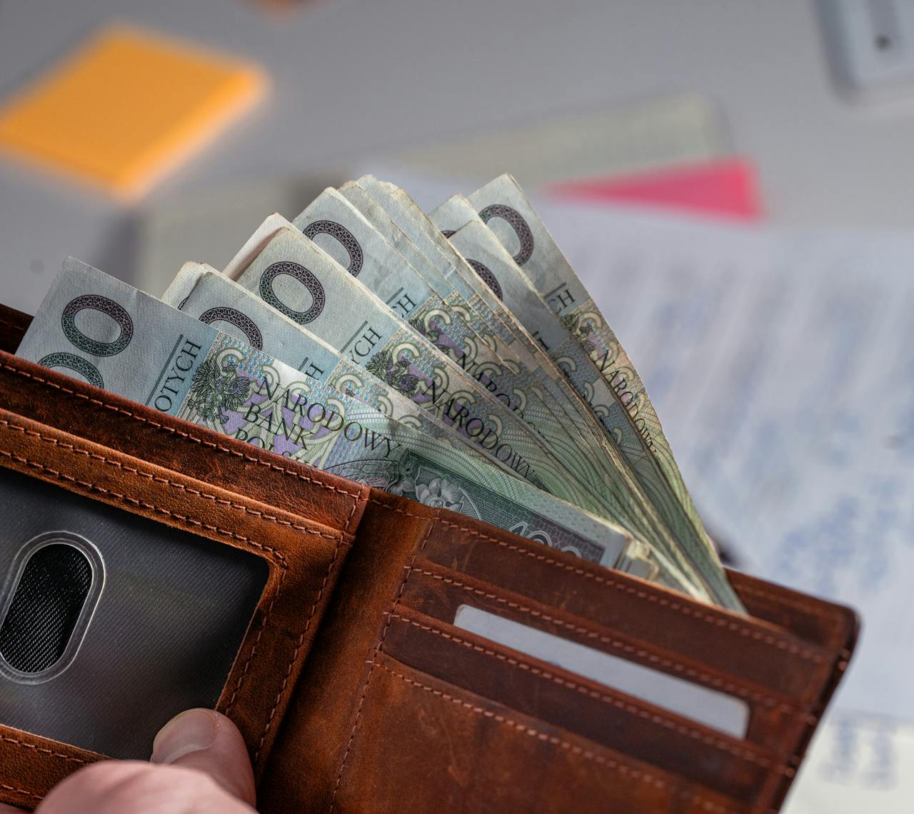services-03 Brown leather wallet containing Polish zloty banknotes on cluttered desk